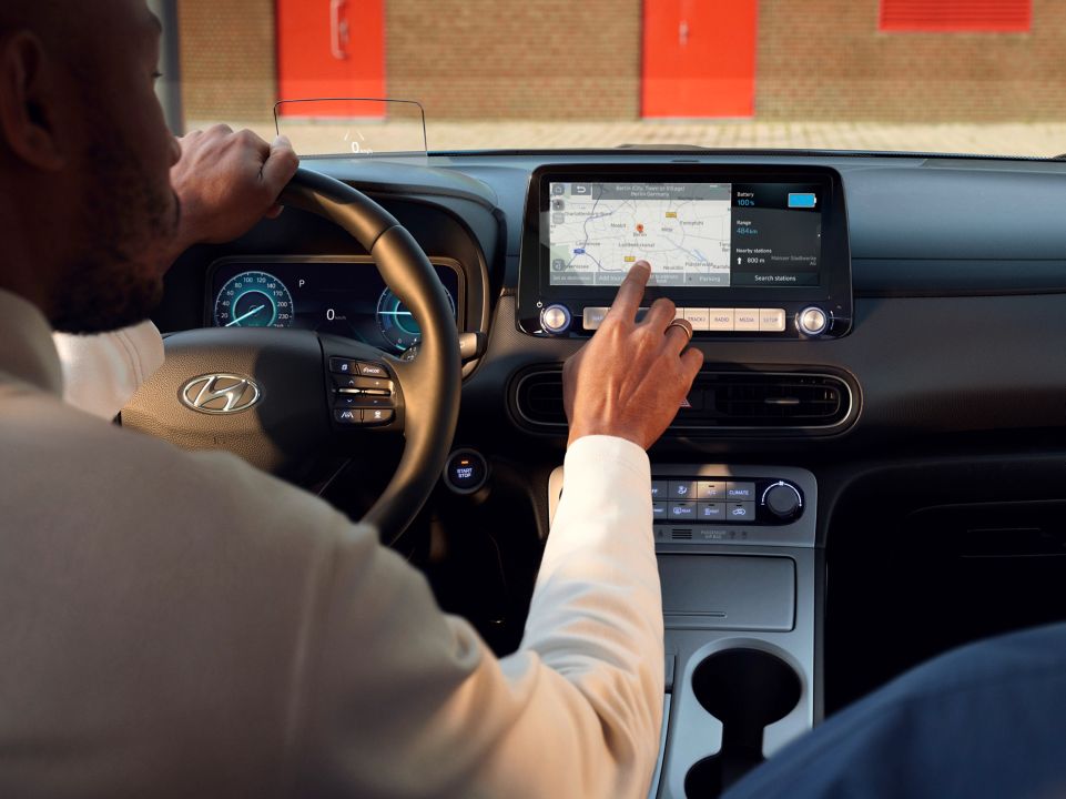 A woman looking at her Hyundai through a coffee shop window, holding her phone in her hands.