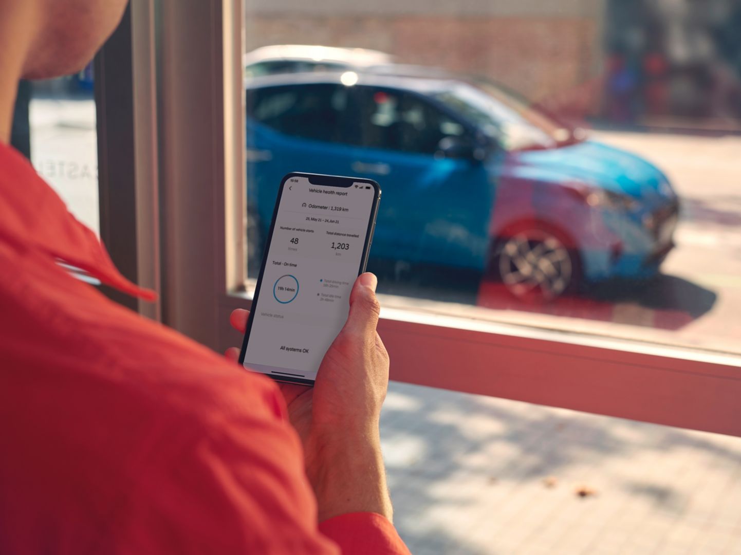 A woman looking at the Hyundai Bluelink App on her smartphone, her car is parked outside.