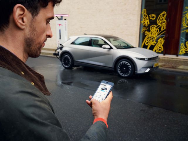 Man walking towards the Hyundai IONIQ 5 electric vehicle using the Bluelink app on his smartphone.