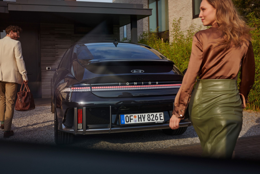 Man with white suit in front of the Hyundai IONIQ 6 and woman with green skirt behind it